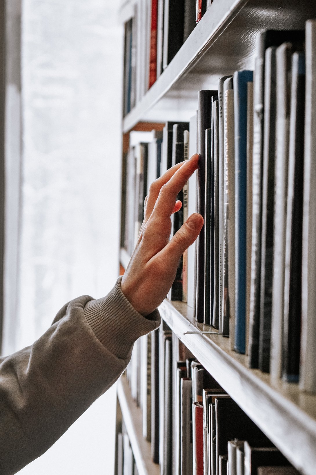 Picture of a hand reaching for a book on a shelf