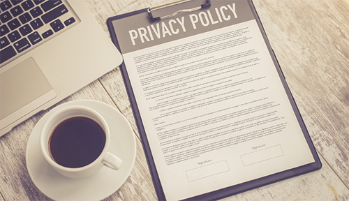 Glimpse of personal computer, privacy document and coffee cup on a light-coloured wooden top