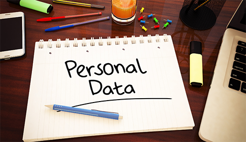 On a dark wooden tabletop, a smarphone, a notepad marked personal data, a glimpse of a laptop, coloured pens and highlighters
