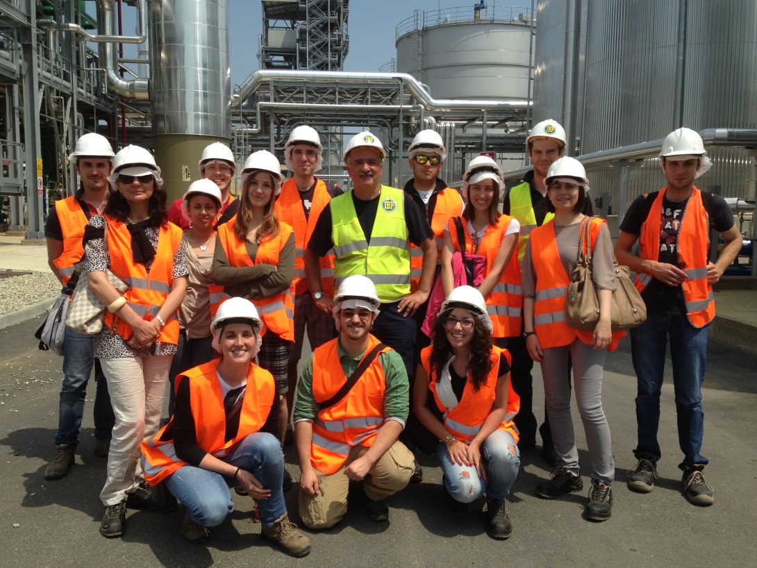 "Group of people wearing orange aprons in a factory yard"